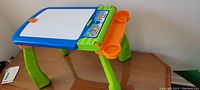 Full image of Vtech Digiart Creative Easel showing the whiteboard surface, four green legs, and orange side trays.
