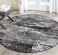 Full view of a round patterned area rug in black and grey laid on light wood floor under natural light.