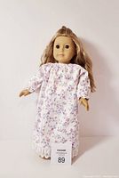 Front view of the American Girl Doll standing, showing full-length floral dress and hairstyle