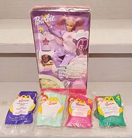 Barbie Dream Glow doll in original box with four sealed McDonald's Barbie collectible toy pouches arranged below.
