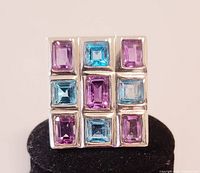 Front-facing photo of the ring showing nine square faceted blue and purple crystals set in a 3x3 grid on the square top of the silver band.