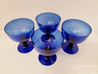 Four cobalt blue glass dessert cups arranged in a pyramid shape showing the rounded bowls and sturdy stems.