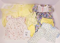 Lot of assorted doll clothing items in medium to large sizes, showing different styles, colors, and patterns arranged flat for display.