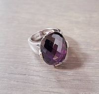 Close-up front angle of the faceted oval purple crystal ring in sterling silver on wooden surface.
