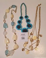 Photo of three necklaces laid flat on white surface showing various bead shapes and coin pendants.