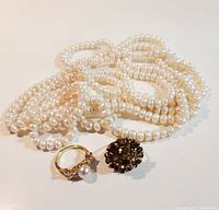 Photo of the pearl necklace placed loose with the two rings in front, showing the detailing of pearls and rings.