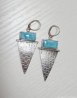 Pair of drop earrings laid flat, showing rectangular turquoise stones set atop textured triangular sterling silver drops with lever-back closures.