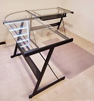 Full view of L-shaped desk with main rectangular glass top and semi-circular return glass surface mounted on black metal frame with X-shaped legs.