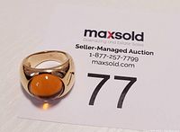 Front view of the gold tone ring with amber cabochon glass set in the center.