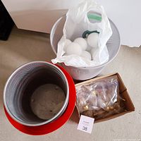 Photo showing red and gray mesh metal waste paper bins, with the gray bin containing 5 white light bulbs in a plastic bag and a green bulb holder. Also, a cardboard box with additional items is partially visible.
