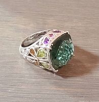 Angled close-up showing large green square-cut central crystal and side colourful smaller crystals