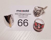 Photo showing all three sterling silver rings arranged near lot number card. Rings include one with gold-tone stripe, one with scale pattern and pointed end, and one with colorful red and pink enamel inlays.