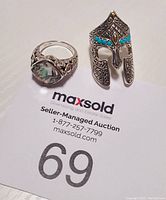 Two rings displayed on MaxSold auction paper, showing sizes and detailed design.