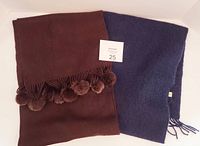 Both scarves laid flat side by side, showing navy and brown colors with pom-poms on brown scarf edge.