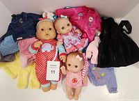 Lot of three vintage dolls in various outfits along with multiple pieces of doll clothing including jackets and dresses.