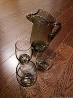 Photo showing the smoky brown glass pitcher standing next to three matching glasses on a wooden floor to display size and color.