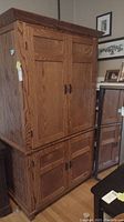 Front view of the solid oak armoire showing the upper and lower cupboards with paneled doors and metal handles.