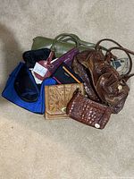 Six bags arranged on beige carpet including two brown Brahmin purses, green croc embossed handbag, blue and black bag, and two vintage tooled leather purses.