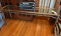 Full view of brass and glass sofa table on wooden floor with a toaster oven placed on top.