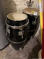 Two black conga drums side by side, one with head and one missing head, with chrome hardware visible.
