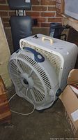 Side view showing the floor fan with circular grille and blue handle, along with the swamp cooler behind.