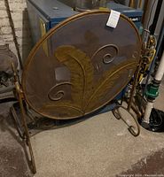 Front and side views of the fireplace screen showing circular mesh wire panel with large leaf design and curved legs with fleur-de-lis detail.