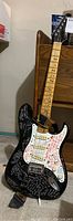 Full view of black Epiphone electric guitar with white pickguard and multicolored signatures on body and neck