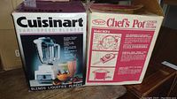 Photo showing original packaging boxes of Cuisinart Vari-Speed Blender and Dayco Chef's Pot Cooker/Fryer/Steamer side by side on wooden surface.