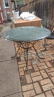 Round metal patio table with clear removable glass top shown on brick patio.
