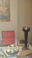 Overall view showing gold electro-plated flatware set in red case, metal and glass ashtray, and tall pedestal with metal top on table.