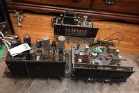 Top view of two vintage tube radios and various electronic parts on floor, showing vacuum tubes and metal chassis.