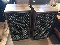 Pair of Sansui SP-1500X floor speakers shown with wood veneer cabinet and front grille covers in diamond pattern fabric.