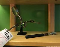 Magnifier stand with articulated arms and clips, and magnetic pickup tool with black handle lying on wooden shelf