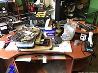 Work table with hardware organizers, assorted parts in trays, a soldering iron setup, and small tools scattered around