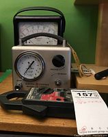 Photo shows three electric testers: a metal casing with pressure gauge and adjustment knob (GE LS-20 halogen leak tester), a black analog multimeter with dial and needle (Triplett 630), and a black clamp meter device (HIOKI 3100).