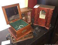 Four wooden jewelry boxes including one with mirrored interior and floral carvings, visible watches and jewelry within and beside the boxes