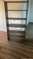 Photo of one painted beige homemade bookcase with six open shelves, rectangular shape, standing on wooden floor