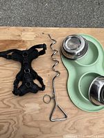 Photo showing small black harness, metal spiral ground stake, and double stainless steel dog bowls inside a mint green silicone mat.