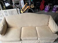 Front view of beige 3-seat sofa with cushioned seats and slightly curved backrest, showing signs of wear and light stains.