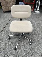 Front view of beige adjustable office chair with cushioned seat and backrest on metal base with casters, showing fabric texture and overall condition.