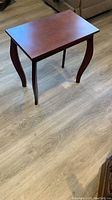 Front-angle photo showing the table's rectangular top and all four curved legs, placed on a wood floor.