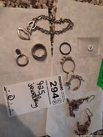 Lot contents showing all 9 pieces: rings, earrings, chain bracelet on white paper with seller tag and 925 mark label visible