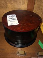 Top view of the round jewellery box showing richly grained wood pattern on lid and part of label.