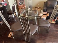 Four metal frame chairs with dark cushioned seats arranged around a glass table, showing overall style and condition.