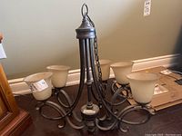 Metal chandelier with five curved arms holding frosted glass bell-shaped shades, hanging chain visible.