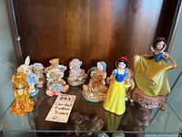 Full view of Cherished Teddies and Disney Snow White figurines arranged on a glass shelf