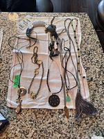 Seven Chico's costume jewelry necklaces laid out flat on a white towel on a granite countertop. Varied designs including beaded, chain link, pendants, braided fabric, and tassel.
