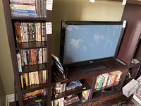 Full view of dark wood shelving unit holding DVDs and books next to a flat screen TV showing the lot contents.
