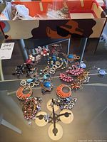 Box with various costume earrings laid out, showing multiple designs and colors including blue, pink, orange, and bronze tones with beads and stones.