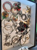 Top-down image showing a variety of costume jewelry earrings including hoops, leaf designs, animal faces, and small studs in silver and gold tones.